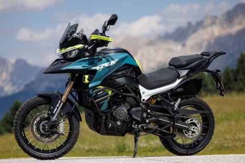 Benelli TRK 902 Xplorer (2026) – Seitenansicht in Petrol/Neongelb mit Kreuzspeichenraedern vor Dolomiten-Panorama