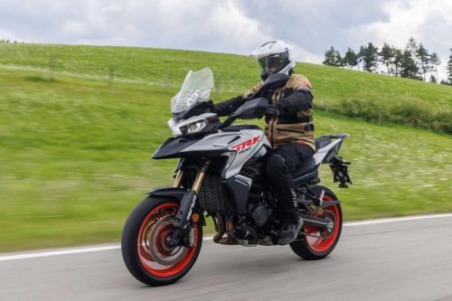 Benelli TRK 902 Stradale (2026) – Fahraufnahme mit Fahrer in Vollmontur beim Herausbeschleunigen aus einer Kurve, gruene Huegellandschaft in den Dolomiten
