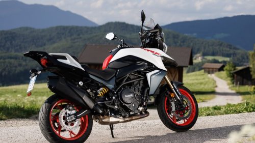 Benelli TRK 902 Stradale (2026) – Seitenansicht in Weiss/Rot vor Suedtiroler Bauernhoefen und Berglandschaft; Kennzeichen am Heck ist lesbar