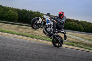 BMW F 450 R 2027 – M Sport in Snaefell Weiß / M Motorsport beim Wheelie auf einer Teststrecke, Fahrer mit rotem Helm
