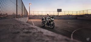 BMW F 450 R 2027 – M Sport in Snaefell Weiß / M Motorsport auf einem Parkdeck mit Basketballkorb in der Abenddämmerung (KI-generiertes BMW-Pressebild)