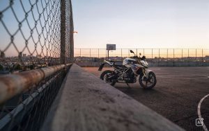 BMW F 450 R 2027 – M Sport in Snaefell Weiß / M Motorsport auf einem Parkdeck neben einem Maschendrahtzaun bei Sonnenuntergang (KI-generiertes BMW-Pressebild)