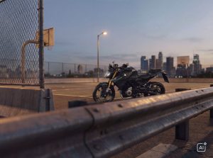 BMW F 450 R 2027 – in Cosmic Black hinter einer Leitplanke vor Skyline und Basketballkorb in der Dämmerung (KI-generiertes BMW-Pressebild)