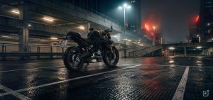 BMW F 450 R 2027 – in Cosmic Black, Seitenansicht auf einem nassen Parkdeck mit Neonlicht bei Nacht (KI-generiertes BMW-Pressebild)