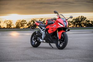 BMW F 450 RR 2027 – Sport in Racing Red, Standaufnahme schräg von vorn auf leerem Asphalt vor Sonnenuntergang und Baumreihe
