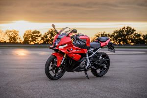 BMW F 450 RR 2027 – Sport in Racing Red, Standaufnahme schräg von vorn mit LED-Tagfahrlicht vor goldenem Abendhimmel