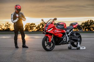 BMW F 450 RR 2027 – Sport in Racing Red auf Montageständer, daneben Fahrer in Lederkombi beim Anziehen der Handschuhe