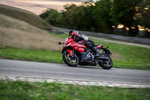 BMW F 450 RR 2027 – Sport in Racing Red in Schräglage durch eine Linkskurve vor grünem Hügel