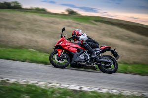 BMW F 450 RR 2027 – Sport in Racing Red in Schräglage durch eine Kurve, Seitenansicht mit Wiese im Hintergrund