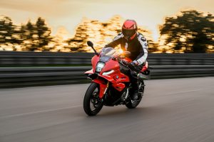 BMW F 450 RR 2027 – Sport in Racing Red in Fahrt bei Sonnenuntergang mit eingeschaltetem LED-Scheinwerfer