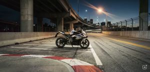 BMW F 450 RR 2027 – M Sport in Snaefell Weiß / M Motorsport unter einer Autobahnbrücke vor nächtlicher Stadtkulisse, Curbs im Vordergrund (KI-generiertes BMW-Pressebild)