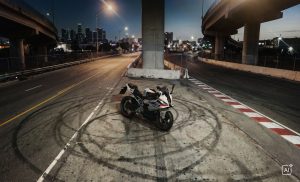BMW F 450 RR 2027 – M Sport in Snaefell Weiß / M Motorsport auf Asphalt mit Reifenspuren, Hochstraße und Skyline im Hintergrund (KI-generiertes BMW-Pressebild)