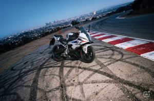 BMW F 450 RR 2027 – M Sport in Snaefell Weiß / M Motorsport auf Asphalt mit Reifenspuren an einer Bergstraße über der Stadt (KI-generiertes BMW-Pressebild)