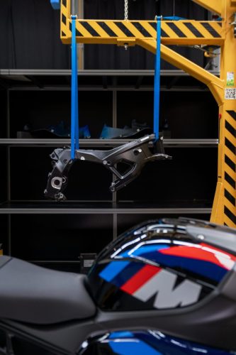BMW M 1000 RR 2027 – neuer M Motorsport Rahmen an Gurten hängend über dem Motorrad, Hochformat