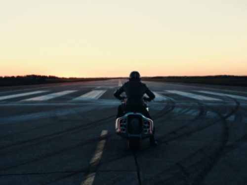 BMW Motorrad Vision K18 – Fahrer entfernt sich auf Startbahn bei Sonnenuntergang mit sichtbaren sechs Endrohren