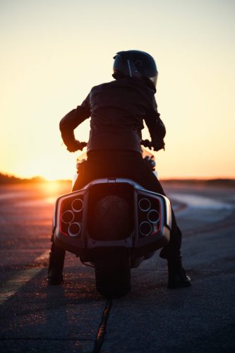 BMW Motorrad Vision K18 – Fahrer-Silhouette von hinten auf Startbahn bei Sonnenuntergang mit sechs Endrohren