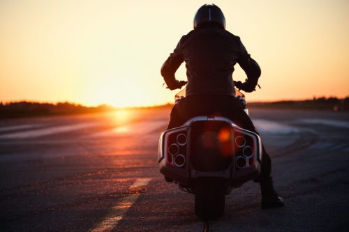 BMW Motorrad Vision K18 – Fahrer auf Startbahn bei Sonnenuntergang, Rückansicht mit langem Schatten und Endrohren