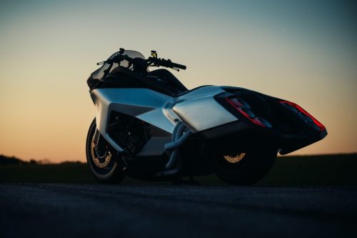 BMW Motorrad Vision K18 – Dreiviertelansicht hinten links auf Startbahn bei Sonnenuntergang mit leuchtenden Rücklichtern