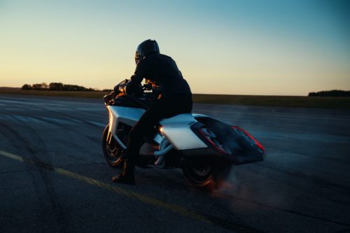BMW Motorrad Vision K18 – Fahrer in Fahrt bei Abenddämmerung, Dreiviertelansicht hinten mit leuchtenden Rückleuchten und Heat-Haze-Effekt