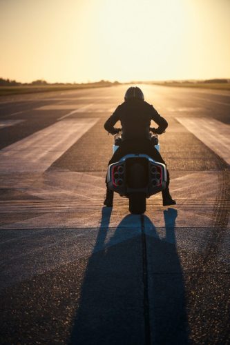 BMW Motorrad Vision K18 – Fahrer-Silhouette von hinten im Gegenlicht auf Startbahn mit sechs Endrohren und langem Schatten