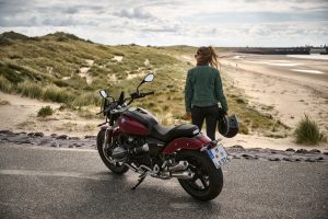 BMW R 12 2025 – Heckansicht schräg mit Fahrerin am Strand, Aventurinrot