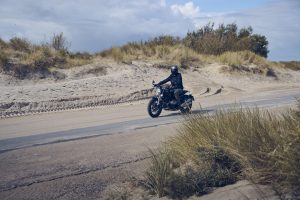 BMW R 12 nineT 2025 – Seitenansicht mit Fahrer auf Dünenstraße, Schwarz