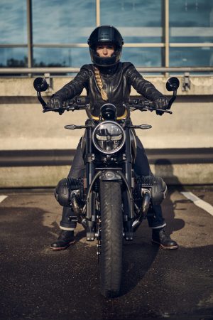BMW R 12 nineT 2025 – Frontansicht mit Fahrerin auf Parkdeck, Avus-Silber