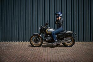 BMW R 12 nineT 2025 – Seitenansicht mit Fahrerin, Wellblechwand, Avus-Silber