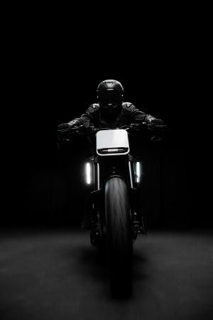 BRABUS Urban-E Fragment Edition 2026 – Fahrer in Schwarz frontal auf dem Motorrad mit eingeschalteten Tagfahrleuchten im dunklen Studio