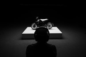 BRABUS Urban-E Fragment Edition 2026 – Fahrer mit Helm vor dem Motorrad auf dem Präsentationspodest, Rückenansicht im Gegenlicht