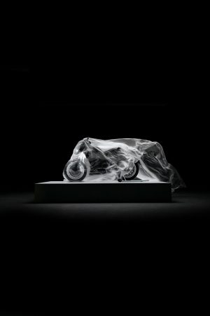 BRABUS Urban-E Fragment Edition 2026 – Unter Folie verhülltes Motorrad auf einem Podest im dunklen Studio