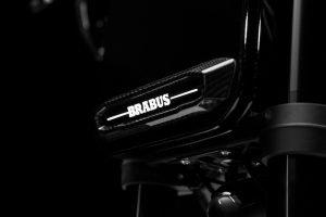 BRABUS Urban-E Fragment Edition 2026 – Beleuchtetes BRABUS-Logo mit Sicht-Carbon-Blende im Dunkeln