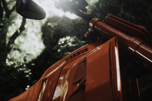 BRABUS URBAN E First Edition Fusion Red 2026 – Detailaufnahme der Tankpartie mit BRABUS-Schriftzug im Gegenlicht zwischen Bäumen