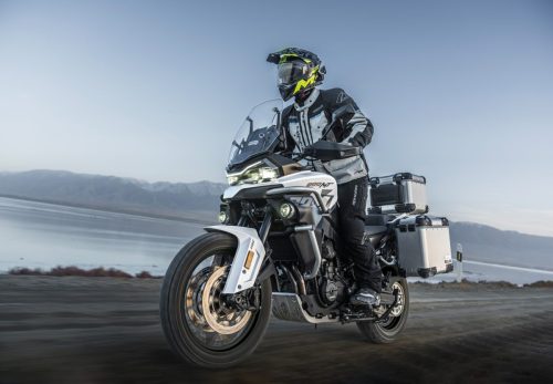 CFMOTO 800MT-ES 2026 in Glacier White – Fahraufnahme mit Fahrer und Aluminium-Seitenkoffern auf der Straße vor Bergkulisse