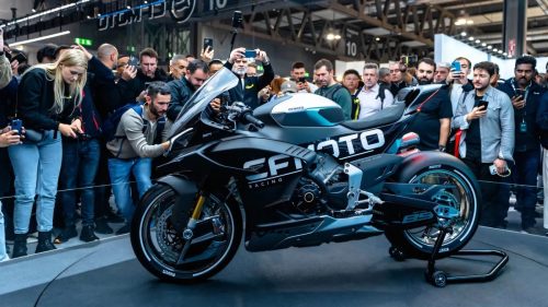 CFMoto V4SR-RR Prototyp in mattschwarzer CFMoto-Racing-Lackierung auf der Bühne der EICMA-Messe, dichte Menschentraube fotografiert das Motorrad von der Seite