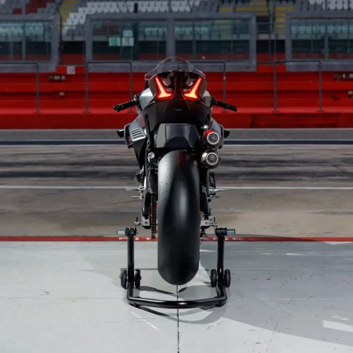 CFMoto V4SR-RR Prototyp von hinten auf der Boxengasse einer Rennstrecke, roter Tribünenhintergrund, LED-Rücklicht und Doppelauspuff sichtbar, Motorrad auf Montageständern