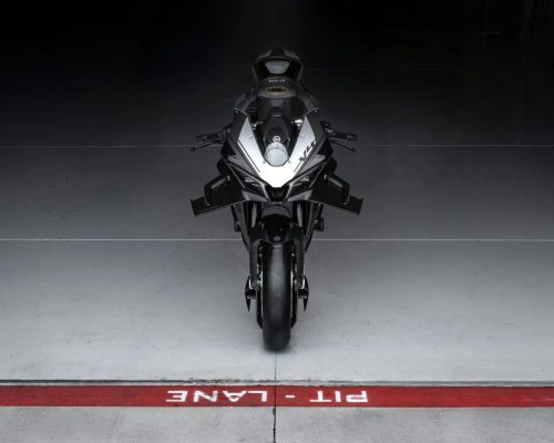 CFMoto V4SR-RR Prototyp Frontalansicht auf einer Pit-Lane-Markierung, symmetrisch ausgefahrene aktive Winglets, silbern-schwarze Lackierung, dunkler Studiohintergrund