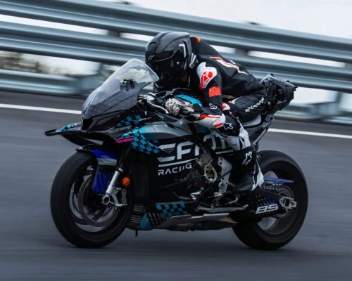 CFMoto V4SR-RR Prototyp in türkis-schwarzer CFMoto-Racing-Lackierung in Schräglage auf der Rennstrecke, Fahrer mit chinesischer Flagge am Ärmel, Startnummer 85