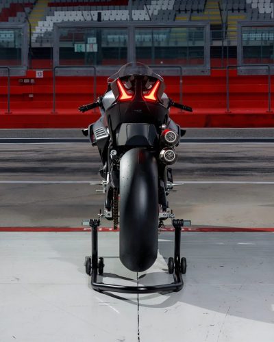 CFMoto V4SR-RR Prototyp von hinten auf der Boxengasse vor roter Tribüne, LED-Rücklicht, runde Doppelauspuffendtöpfe, auf Montageständern abgestellt