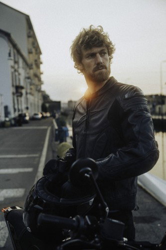 DAB 1a BRABUS 2026 – Fahrer mit lockigem Haar in schwarzer Lederjacke am Navigli-Kanal im Gegenlicht