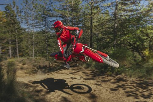 Ducati Desmo450 EDS 2027 in Ducati Red – Fahrer beim Sprung über einen Waldweg mit Bewegungsunschärfe und Schattenwurf am Boden