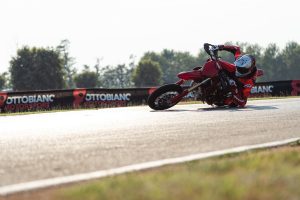 Ducati Desmo450 SM 2027 – Supermoto-Fahrer in tiefer Schräglage auf der Rennstrecke vor Werbebanden