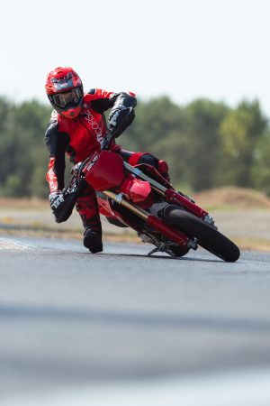 Ducati Desmo450 SM 2027 – Fahrer in Rot mit ausgestelltem Bein in der Kurve, Hochformat