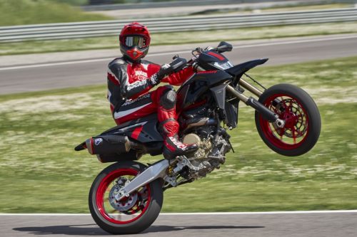 Ducati Hypermotard 698 Mono Nera 2027 – Wheelie in Seitenansicht auf Rennstrecke, Fahrer in Ducati-Corse-Kombi, Superquadro-Mono-Motor und rote Räder gut sichtbar