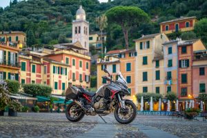 Ducati Multistrada V4 S Grand Tour 2027 – in grauer Grand-Tour-Lackierung mit roten Akzenten und Seitenkoffern vor den bunten Häuserfassaden von Portofino