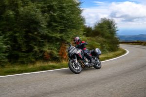 Ducati Multistrada V4 S Grand Tour 2027 – Fahraufnahme in Schräglage in einer Kurve mit Blick aufs Meer, mit Seitenkoffern