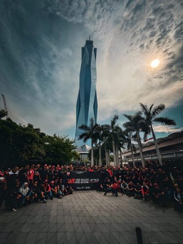 Ducati #WeRideAsOne 2026 – Gruppenfoto in Malaysia vor modernem Wolkenkratzer mit WeRideAsOne-Banner bei Sonnenuntergang