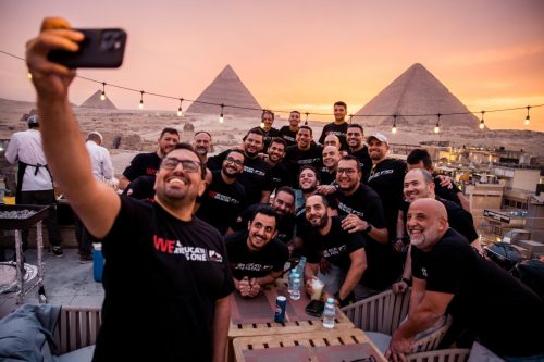 Ducati #WeRideAsOne 2026 – Gruppenselfie der Ducatisti auf Dachterrasse bei Sonnenuntergang vor den Pyramiden von Gizeh in WeRideAsOne-T-Shirts