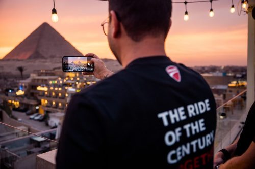 Ducati #WeRideAsOne 2026 – Ducatist fotografiert die Pyramiden von Gizeh mit Smartphone bei Sonnenuntergang, The Ride of the Century T-Shirt mit Ducati-Logo