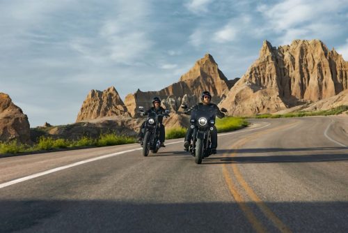 Harley-Davidson Deadwood – zwei Fahrer auf mattschwarzen Cruisern auf kurviger Landstraße durch die Felsformationen der Badlands